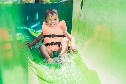 A boy in a life jacket slides down from a slide in a water park.