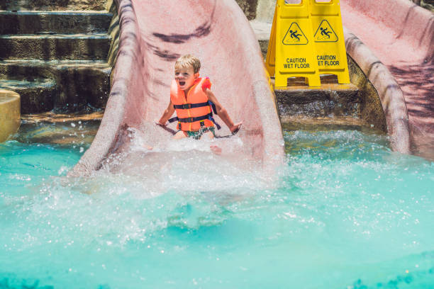 ein junge in einer schwimmweste rutscht von einer rutsche in einem wasserpark - amusement park family water slide child stock-fotos und bilder