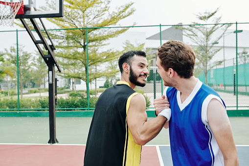 Cheerful multi-ethnic basketball players shaking hands after playing game outdoors