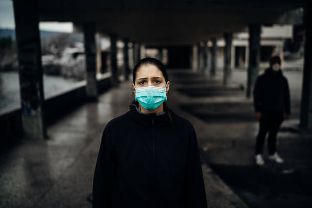 Person wearing a protective mask to prevent contagious disease spread.Life during epidemic/pandemic.Two people in abandoned place standing with distance.Sad woman affected by the infection. stock photo