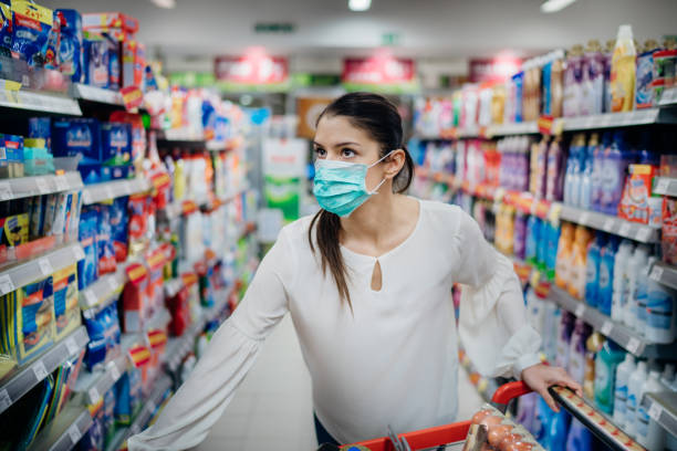 Woman wearing protective mask preparing for virus pandemic spread quarantine.Finding the right products on the shelves in the supermarket.Hygiene, cleaning and disinfection products.Budget buying. stock photo