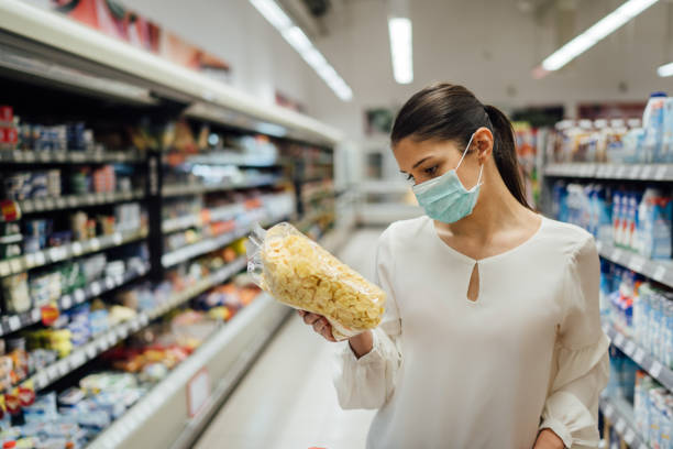 Shopping during an epidemic.Buyer wearing a protective mask.Nonperishable smart purchased household pantry groceries.Pandemic quarantine preparation.Dry goods and nutritional foods shopping.Expiration compras durante una epidemia. comprador con una máscara protectora. los alimentos de despensa para el hogar comprados inteligentes no perecederos. preparación de cuarentena pandémica. productos secos y alimentos nutricionales de compras. expiración