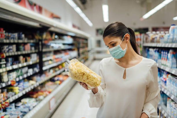 Shopping during an epidemic.Buyer wearing a protective mask.Nonperishable smart purchased household pantry groceries.Pandemic quarantine preparation.Dry goods and nutritional foods shopping.Expiration stock photo