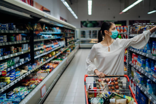 Woman with hygienic mask shopping for supply.Budget buying at a supply store.Emergency to buy list.Shopping for enough food and cleaning products.Preparation for a pandemic quarantine due to covid-19 stock photo