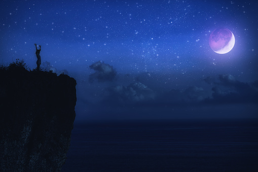 Silhouette of a woman with milky way stars above the ocean horizon.