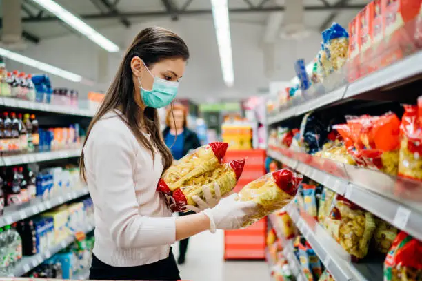 Photo of Buyer wearing a protective mask.Shopping during the pandemic quarantine.Nonperishable smart purchased household pantry groceries preparation.Woman buying few pasta packages.Budget pastas and noodles.