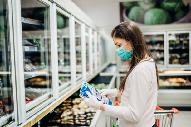 Woman wearing face mask buying in supermarket.Panic shopping during Coronavirus covid-19 pandemic.Budget buying at a supply store.Buying freezer smart purchased household pantry groceries stock photo