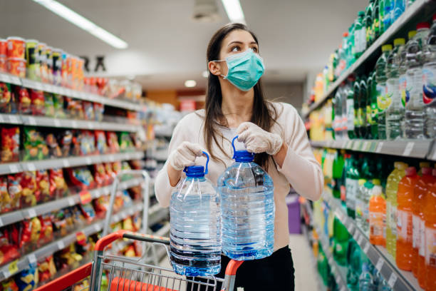 Woman wearing face mask buying bottled water in supermarket/drugstore with sold-out supplies.Prepper buying bulk supplies due to Covid-19 or Coronavirus and panic buying concept. stock photo