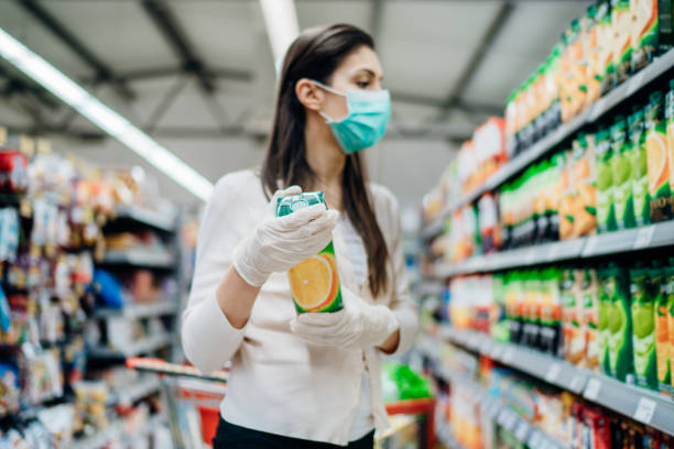 Natural source of vitamins and minerals.Orange juice.Vitamin C.Woman wearing face mask buying in supermarket.Woman preparing for pathogen virus pandemic quarantine.Preventive measures and protection stock photo
