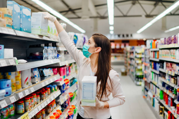 Woman wearing mask and gloves buying baby formula due to Covid-19 or Coronavirus and panic buying.Preparation for a pandemic quarantine.Shopping for infant formula,baby food supply shortage.Hoarding stock photo