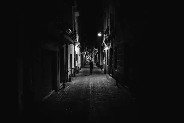 Woman walking alone in the street late at night.Narrow dark alley,unsafe female silhouette.Empty streets.Woman pedestrian alone.Police hour.Assault situation,violence against women concept.