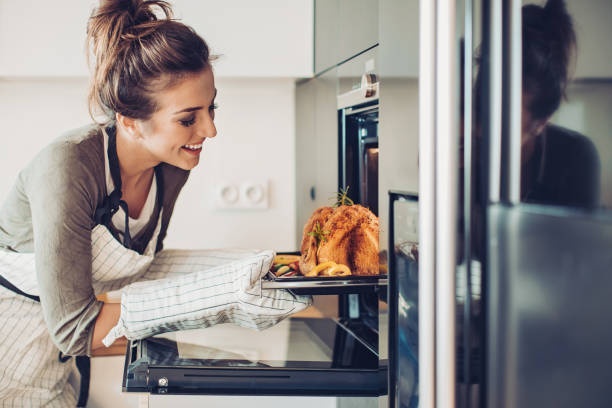 Young woman baking turkey for Thanksgiving Smiling woman pulling roasted turkey out of the oven oven stock pictures, royalty-free photos & images