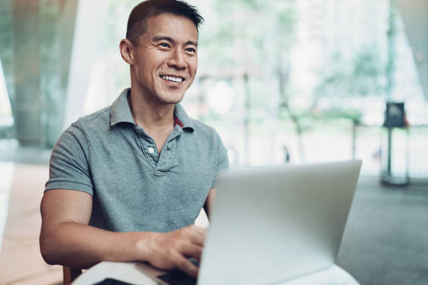 Smiling Asian ethnicity man with laptop in cafe