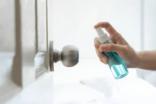 Hand applying alcohol spray to door, doorknob bedroom for protect coronavirus, germs, virus, and cleaning at the house with with background. Prevention covid-19 epidemic.