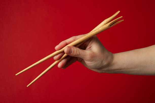istock Female hand with chopsticks on red background, close up 1218509761
