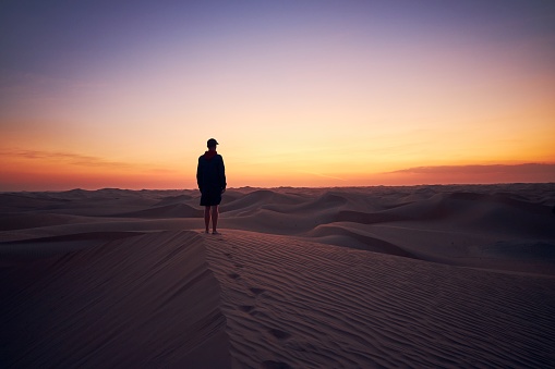 Lonely man standing on sand dune in the middle of desert at dusk. Abu Dhabi, United Arab Emirates