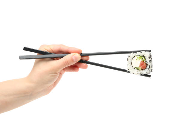 箸を持つ女性の手は、白い背景に孤立した寿司ロールを保持します - herb plant rice white rice ストックフォトと画像