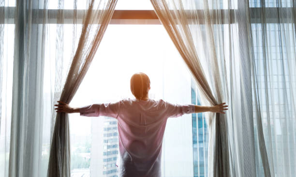 istock Woman opening curtains and looking out 1218513185
