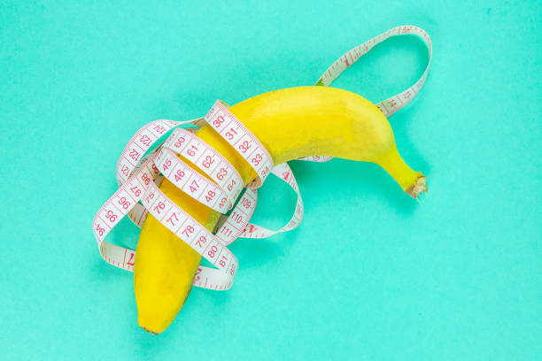 istock Banana with tape for measuring figure. Centimeter ruler spinned around fruit. Tape wrapped around banana isolated on mint background. Weight loss, healthy food and slim body concept 1218515295
