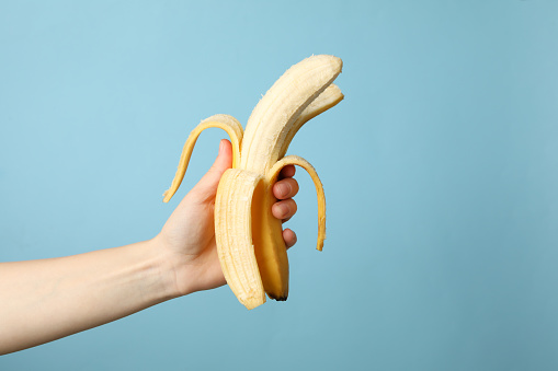 Female hand holds banana on blue background. Fresh fruit