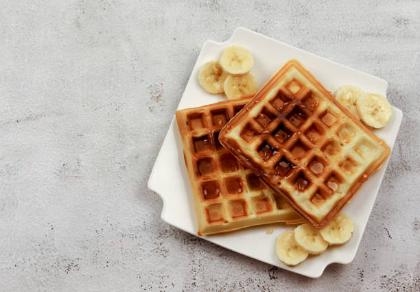 istock Viennese waffles with banana slices and honey on a white rectangular plate on a light gray background 1218517967