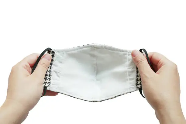 First-person view of hands holding cloth face mask isolated on white background. Due to lack of medical protective face masks during Coronavirus (COVID-19) pandemic, people sew their own cotton masks.