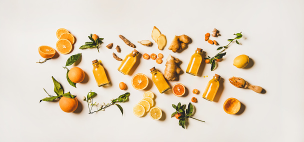 Immune boosting natural vitamin health defending drink to resist virus. Flat-lay of fresh turmeric, ginger and citrus juice shots over white background, top view. Vegan Immunity system booster