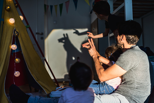 Bonding between single father and small children. Father, brother, sister and baby are playing with shadows at home. There is tent, lights and good mood. Fun moments during COVID-19 isolation.