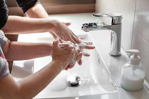 Madre enseñando a su hija cómo lavarse las manos adecuadamente con jabón para prevenir el coronavirus photo