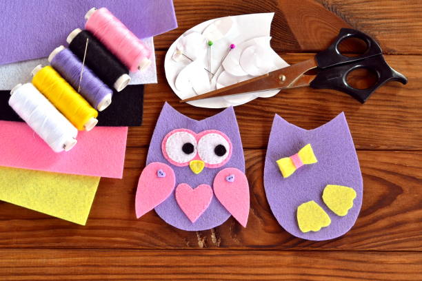 istock Kit for sewing a felt owl, paper templates, felt sheets, scissors, thread, needle, pins on a brown wooden background. Felt hand sewing projects for kids. Sewing step by step 1218526024