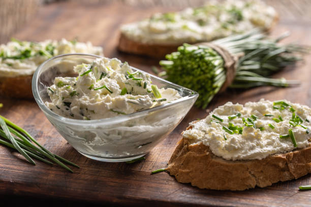 un bol de fromage à la crème maison tartinade avec de la ciboulette hachée entourée de tranches de pain avec de la tartinade et un bouquet de ciboulette fraîchement coupée. - fromage frais photos et images de collection