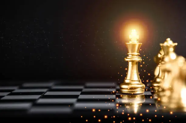 Gold color chess pieces on chessboard, focused on King piece. Business strategy concept. Business teamwork concept.