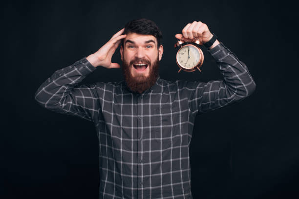 istock young man with beard holding alarm clock over black backgorund 1218530546