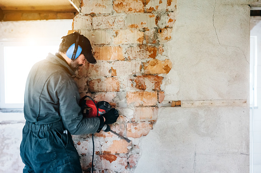 Trabajador maduro demoliendo pared con taladro en casa photo
