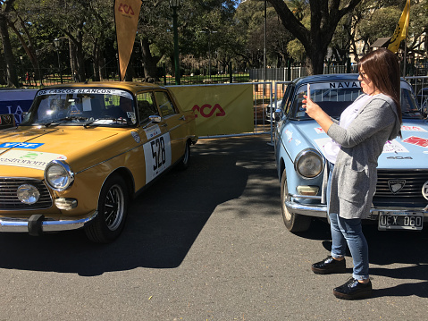 Buenos Aires, Argentina - September 14, 2019: Woman photographing with smartphone parked Peugeot vintage car in exhibition for the public in the street before the start of the Historic Grand Prix event organized by the Argentine Automobile Club, an organization created to represent the interests of motor car users countrywide