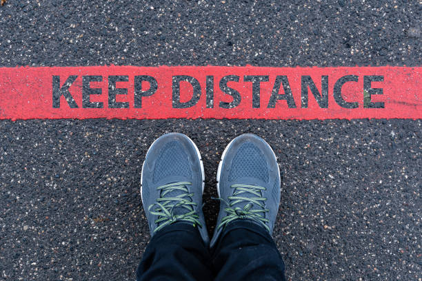 istock man in sneakers standing next to a red line with text KEEP DISTANCE 1218539900