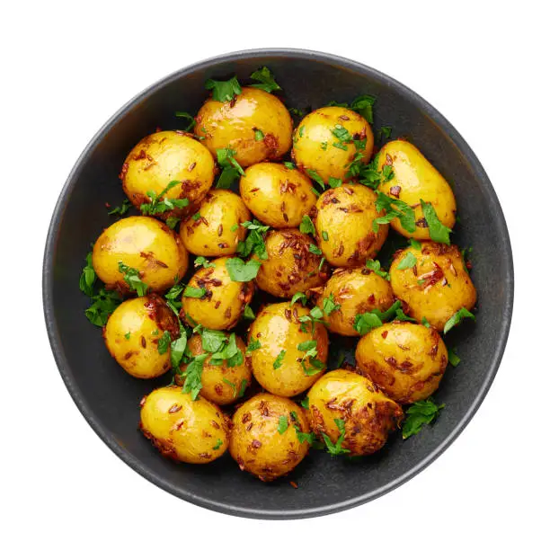 Jeera Aloo in black bowl isolated on white background. Jeera Aloo is indian cuisine dish with baby potatoes, jeera seeds and coriander. Isolate. Top view