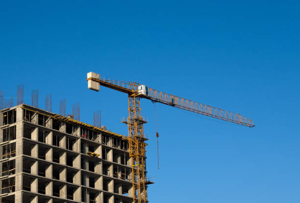 istock Tower crane constructing a new residential building at a construction site against blue sky. Renovation program, development, concept of the buildings industry. 1218541188