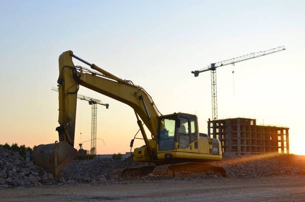 istock Excavator with a large iron bucket on a construction site during road works. Backhoe dig the ground for the foundation, laying storm sewer pipes. Installation of water main systems. 1218541366