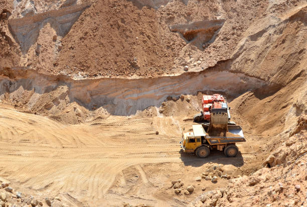 istock Excavator developing the sand on the opencast and loading it to the heavy dump truck. Processing of loose material in mining quarry. Drill, breaking, processing plant, crushing and screening - Image 1218541521