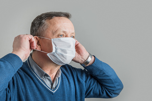 Adult man puts on medical surgical mask to protect against virus Covid 19. Space for text. Prevention of Coronavirus.
