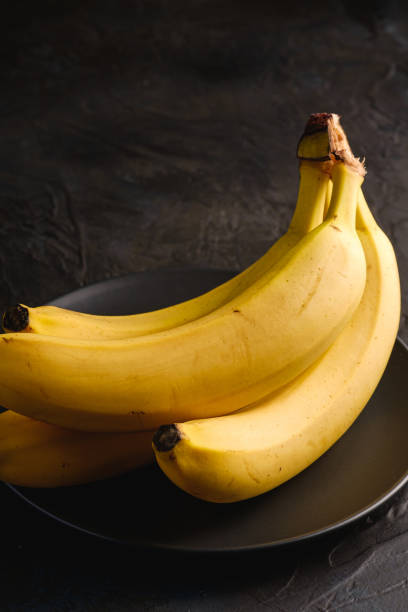 istock Banana fruits in black plate on dark textured background, angle view macro 1218544152