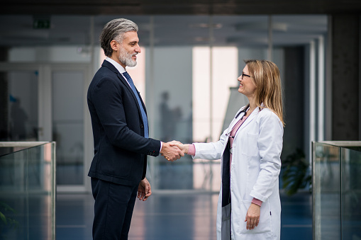 Unrecognizable doctor talking to pharmaceutical sales representative, shaking hands.