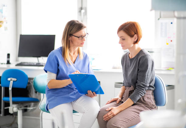 A dentist talking to woman in dentist surgery, a dental check-up. A dentist with clipboard talking to woman in dentist surgery, a dental check-up. annual event stock pictures, royalty-free photos & images