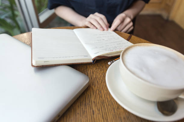 mains de femme avec la tasse de café, l’ordinateur portatif et l’ordinateur portable prenant des notes pour affaires sur la table, se ferment vers le haut - connection usa coffee cup mug photos et images de collection