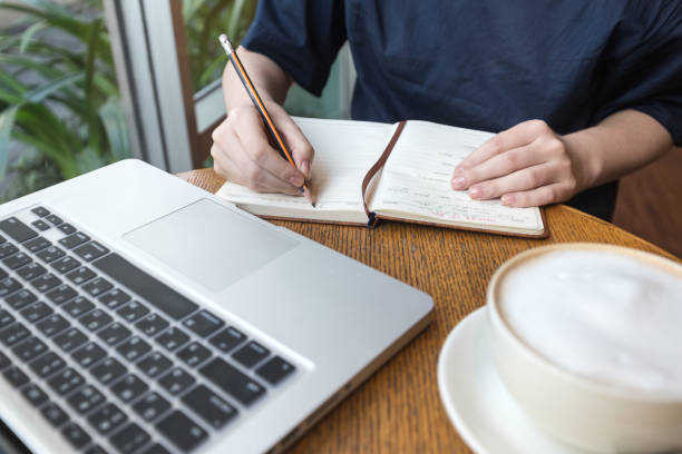 istock Woman's hands with coffee cup, laptop and notebook taking notes for business on table, close up 1218553021