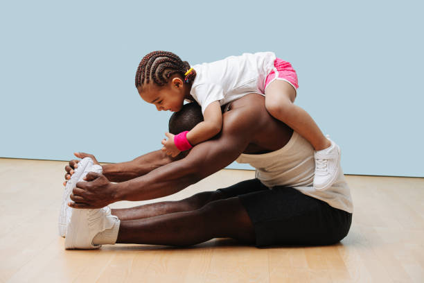 Daughter climbes on her father, as he stretches on the floor stock photo