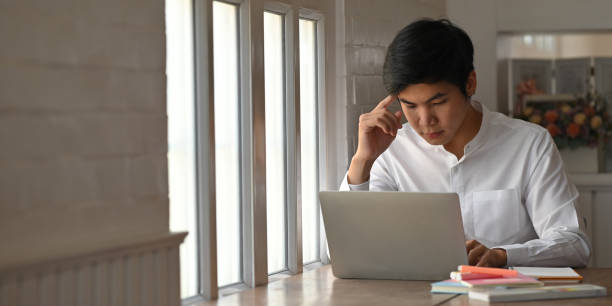 istock Man in white shirt concentrated on computer laptop while sitting at the working table over luxury and modern living room as background. 1218554478