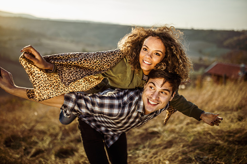 Young happy couple having fun while piggybacking with their arms outstretched in autumn day.