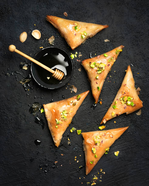 Arabe phyllo sweets. Feta cheese Phyllo Triangles pies with honey and pistachios, selective focus. Cooking sweets turkish, or arabic traditional ramadan pastry dessert on a dark background. Top view.